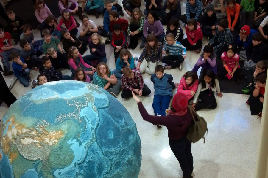 A tour guide shows children a large model of Earth