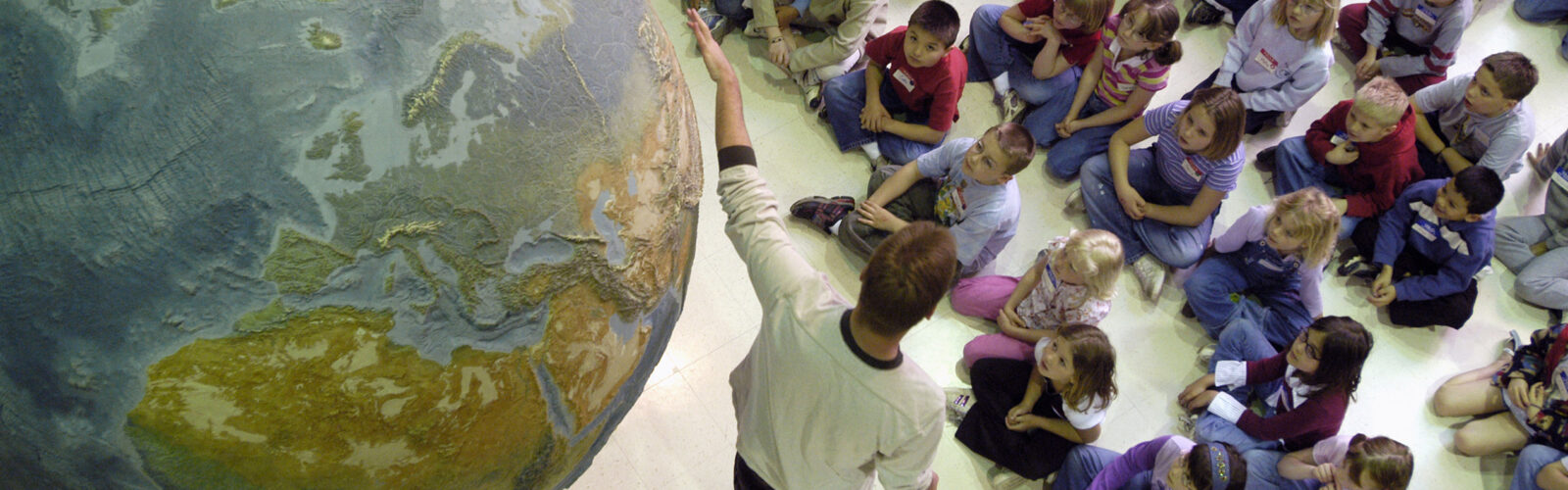 A tour guide shows children a large model of Earth